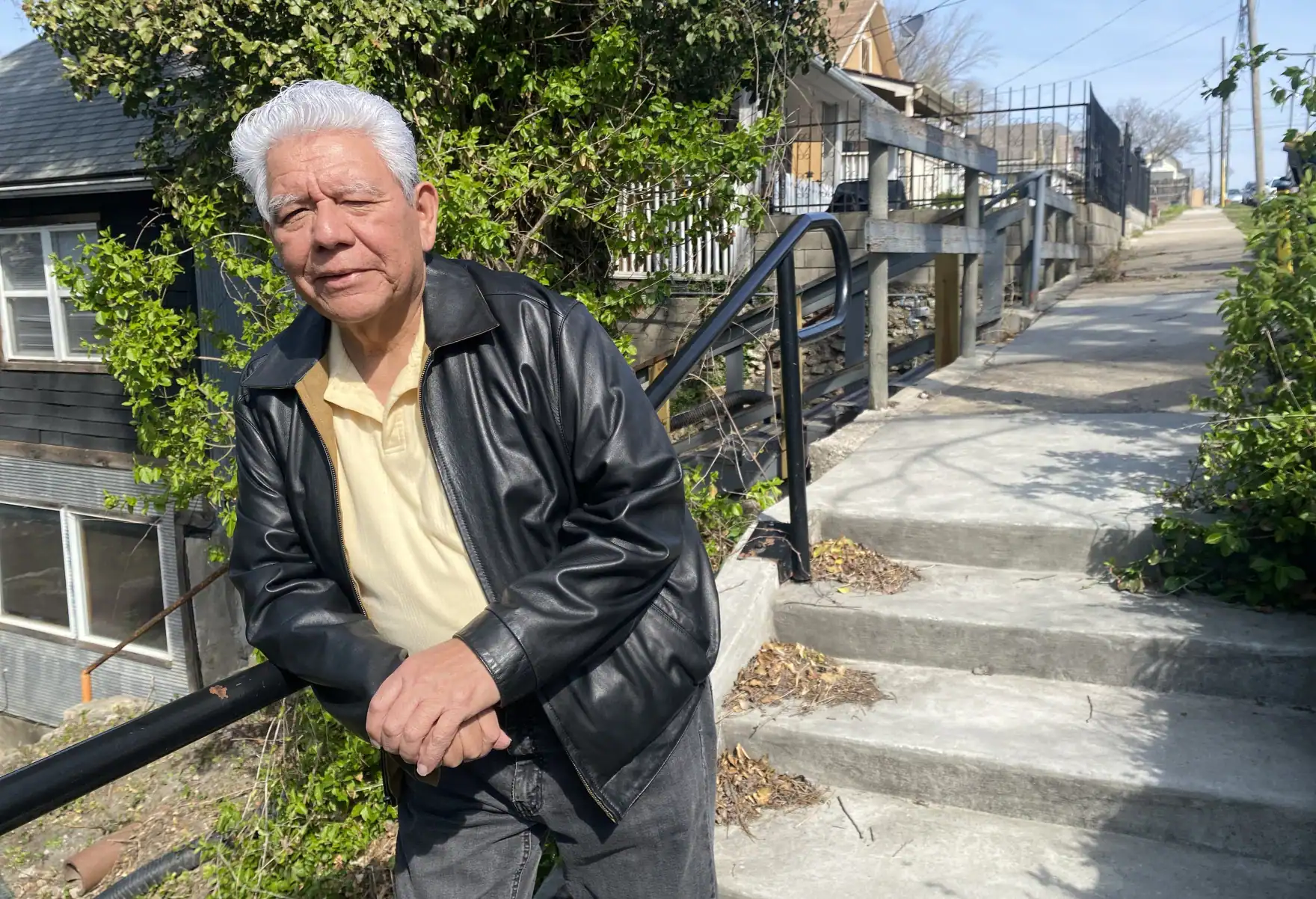 Elder Latino man leaning on railing outdoors in Kansas City neighborhood.