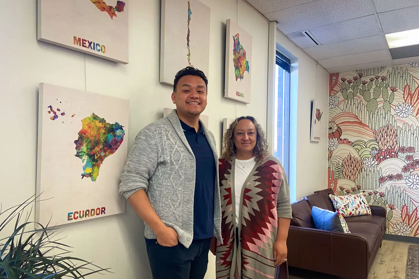 Latino man and woman in a community health center with colorful Latin American map art.