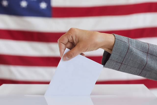 Ballot being cast in front of an American flag, symbolizing voting and political participation.