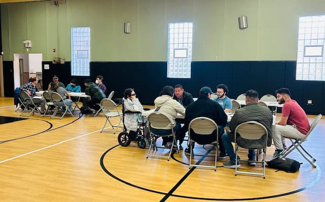 Community members engaging in a discussion during a collaborative event in a gymnasium.