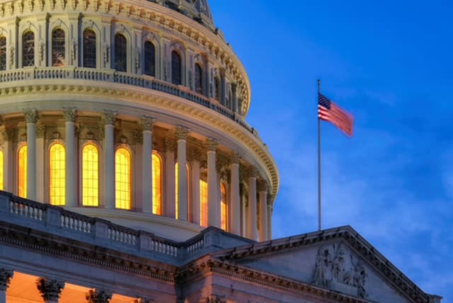 US Capitol building illuminated at sunset with American flag flying high.