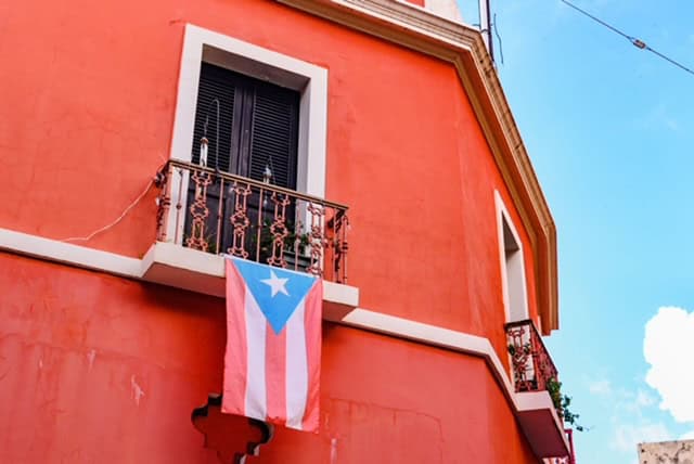Puerto Rican flag hanging from a vibrant orange building under a clear blue sky.