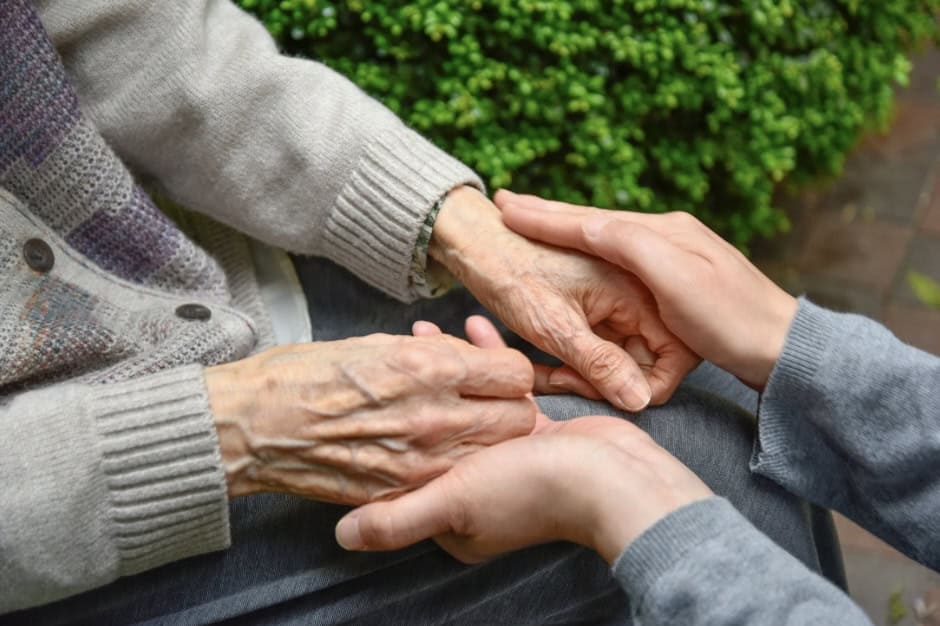 Elderly hands holding caregiver’s hand, emphasizing dementia care and support.