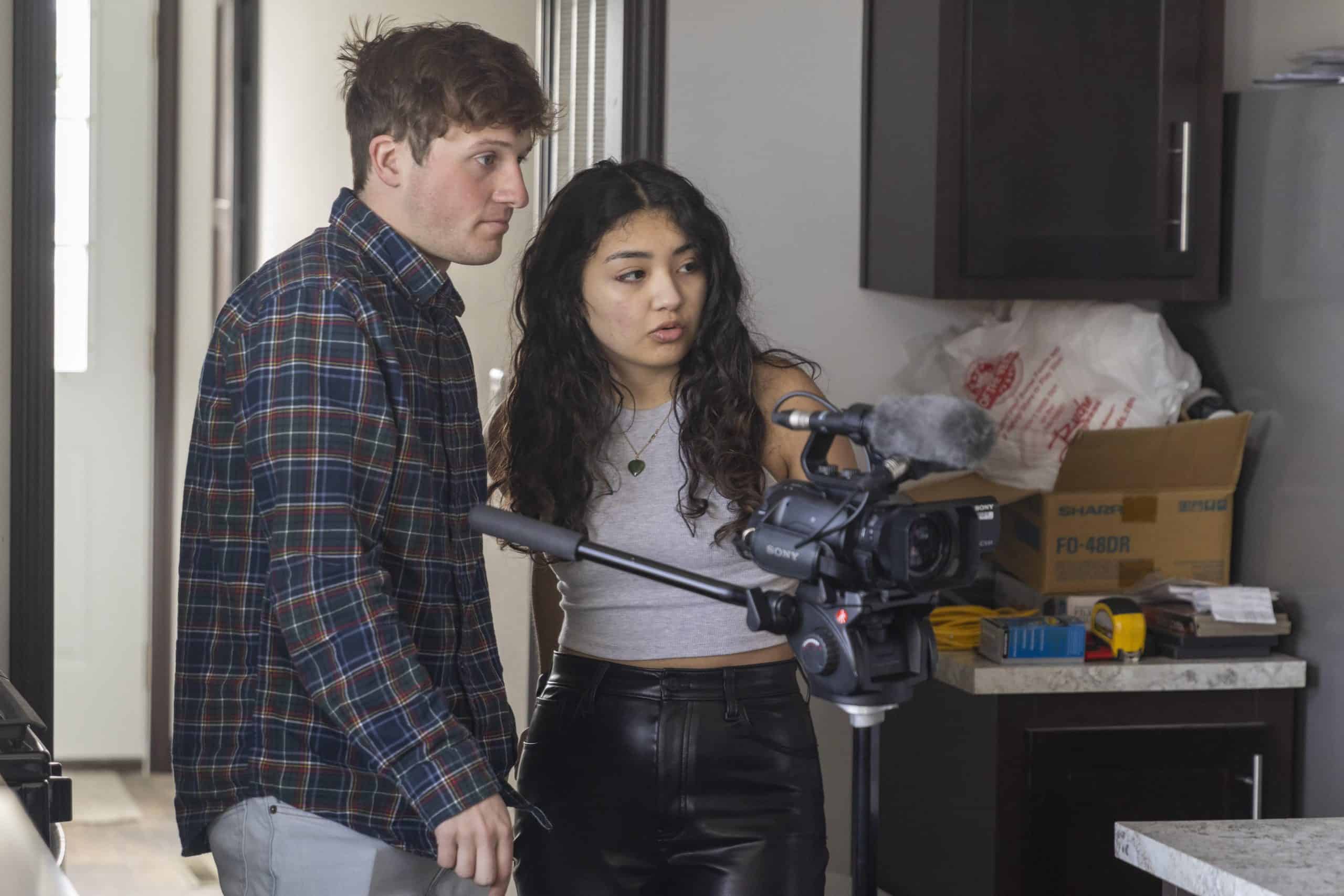 A woman and a man operating a professional video camera in a modern kitchen setting.