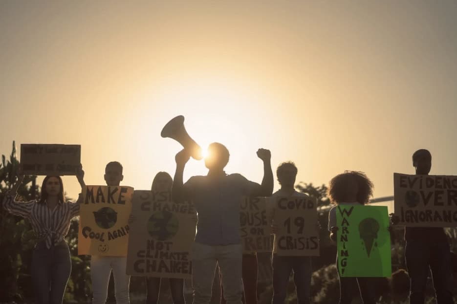 Protesters holding signs during a demonstration at sunset, advocating for social change and awarenes.