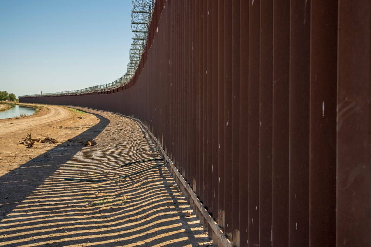 Border wall stretches along the Rio Grande river in a desert landscape.