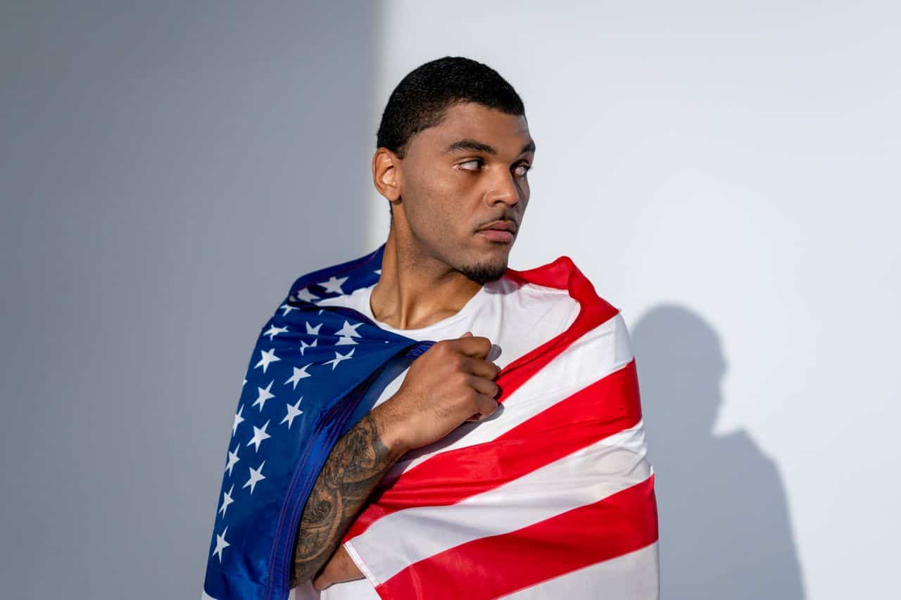 Young man draped in American flag looking to the side.