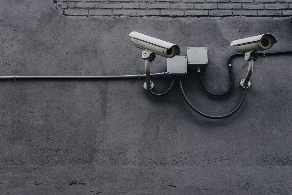Two security cameras mounted on a gray wall for surveillance.