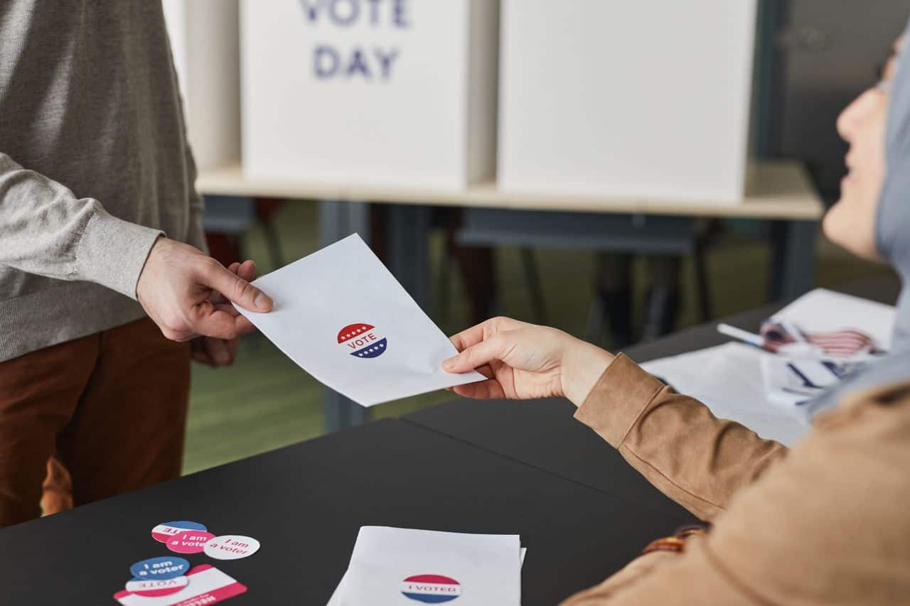 Person submitting ballot with election logo at voting station.