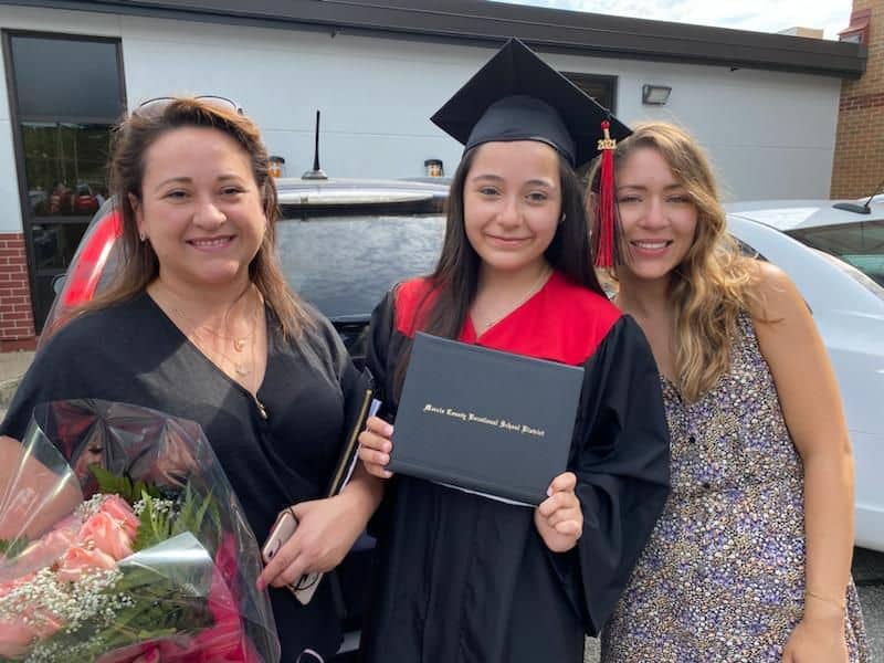 Latina graduate in cap and gown with family celebrating graduation.