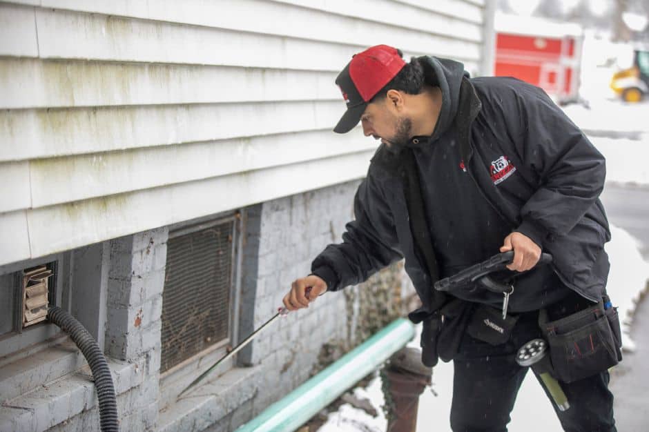 Latino man inspecting building foundation with a measuring tape outdoors.