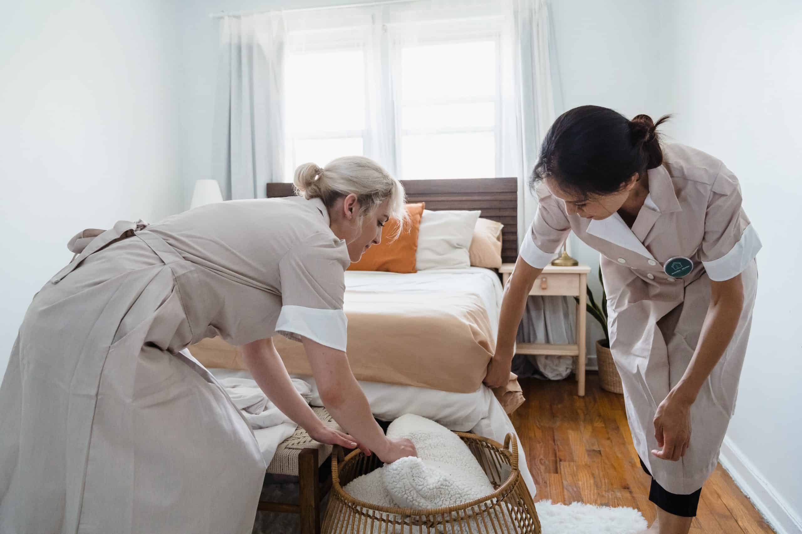 Cleaning staff disinfecting a bed in a hotel room, promoting hygiene and safety.