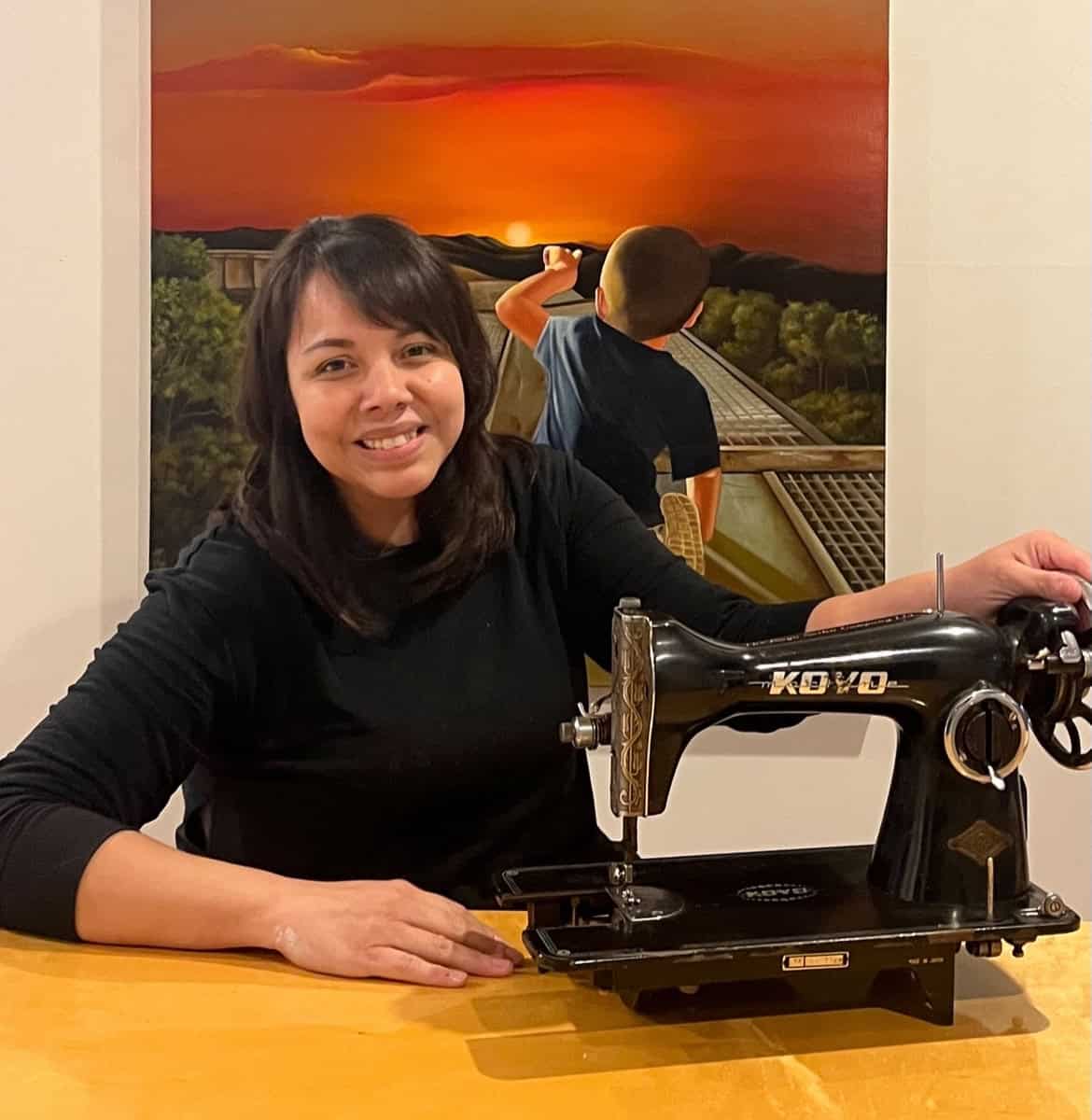 Sewing machine with woman and sunset mural in background, vibrant colors.