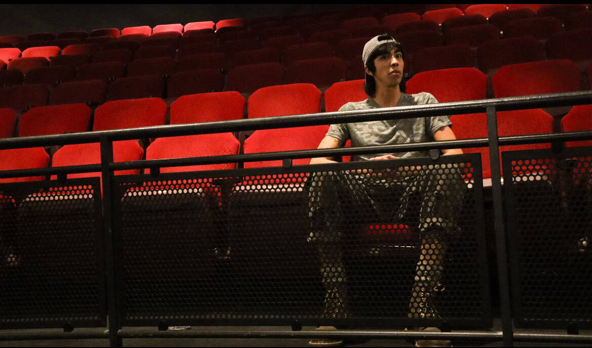 A woman sitting alone in an empty theater with red seats.