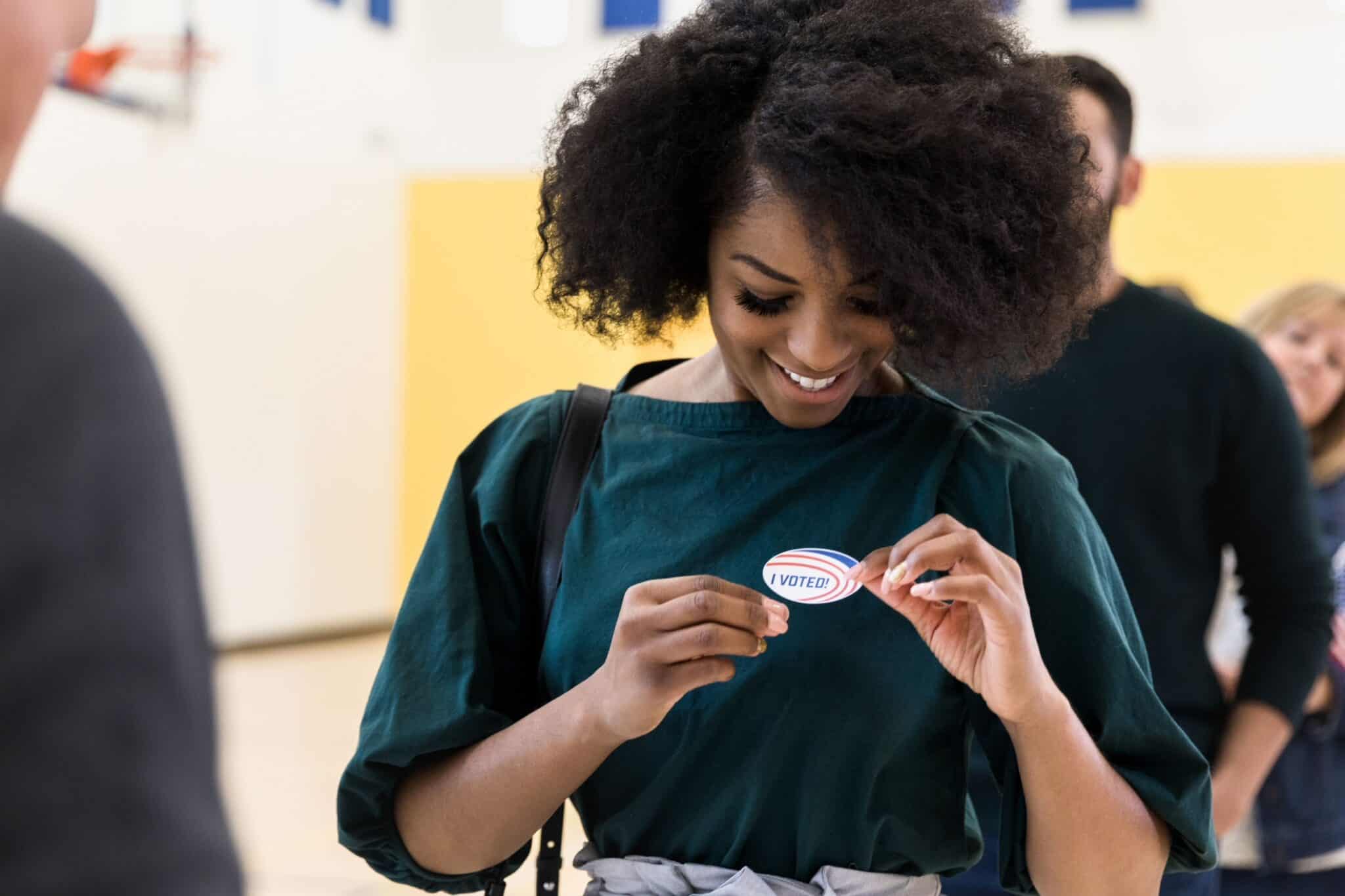 Voter holding an "I Voted" sticker at a diverse election event.