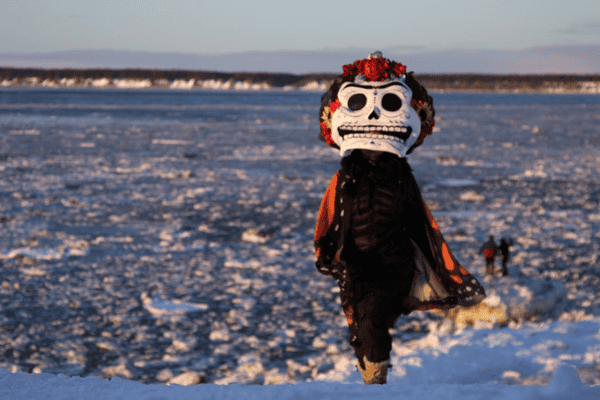 Colorful skeleton doll celebrating Día de los Muertos in icy Alaskan landscape.