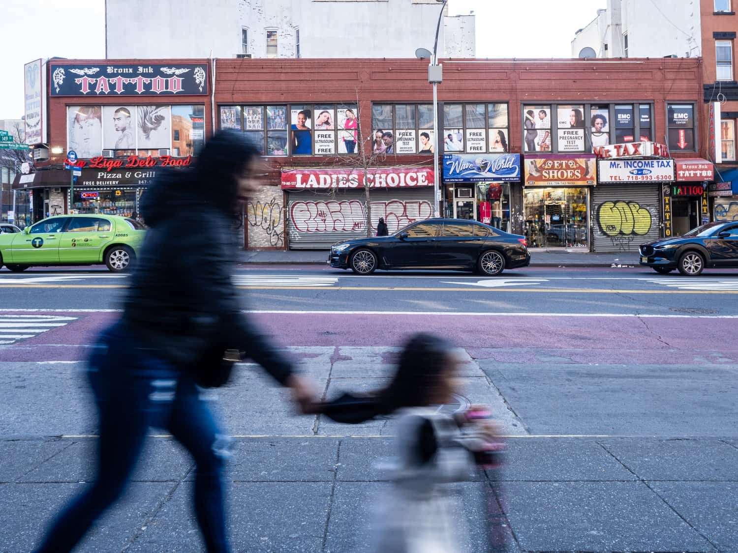 Urban storefronts with signs for tattoo shops, pizza, and shoes.