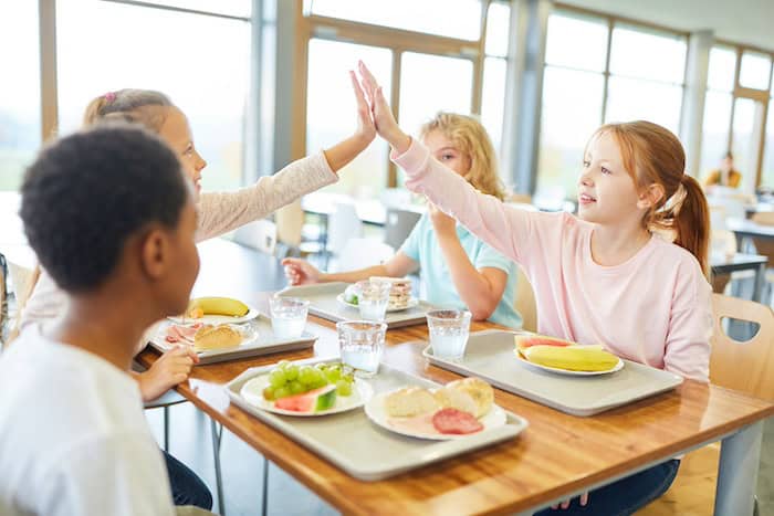 High school students sharing a high-five during lunch in a school cafeteria.