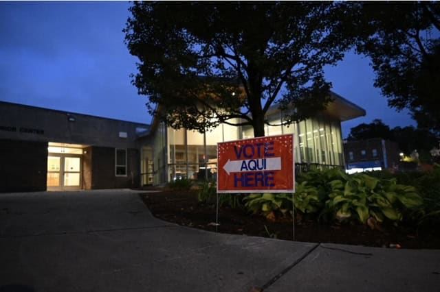 Early voting site in Connecticut with a "Vote Here" sign at dusk.