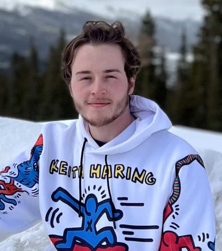 Young man in snow wearing hoodie with "Keith Haring" artwork and vibrant designs.