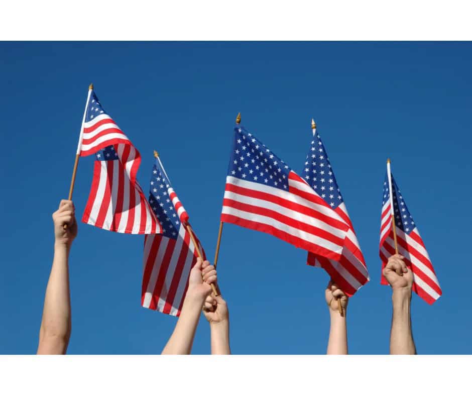 American flags being waved by diverse hands against a clear blue sky, symbolizing patriotism and uni.