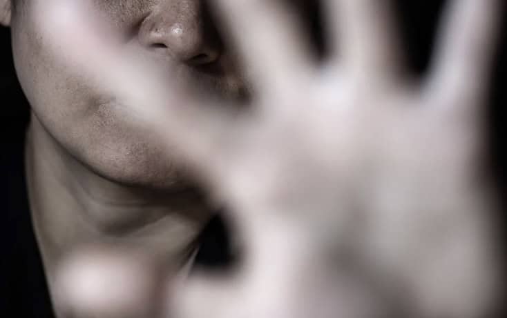 A woman covering her face with her hand, expressing distress or fear related to domestic violence.