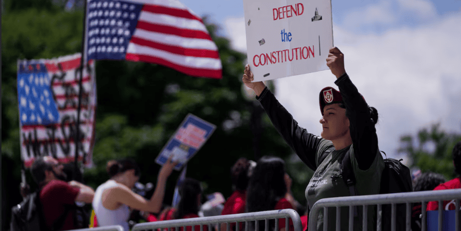 Protestor holding a sign that says "Defend the Constitution" at a rally supporting democracy.