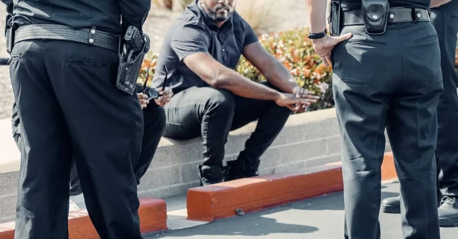 Police officers talking to a man sitting on a curb in a parking lot.