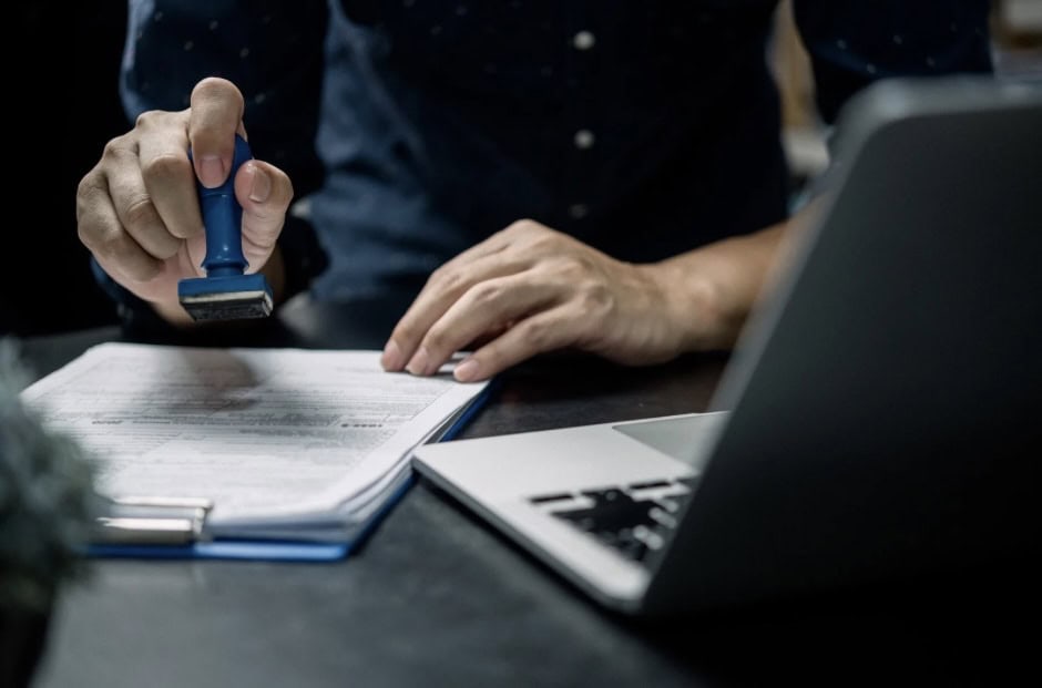 Person stamping documents with a laptop nearby, immigration process, official paperwork, legal proce.