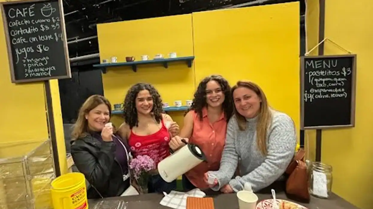 A woman and three girls smiling at a café counter with a yellow background, holding a large coffee m.