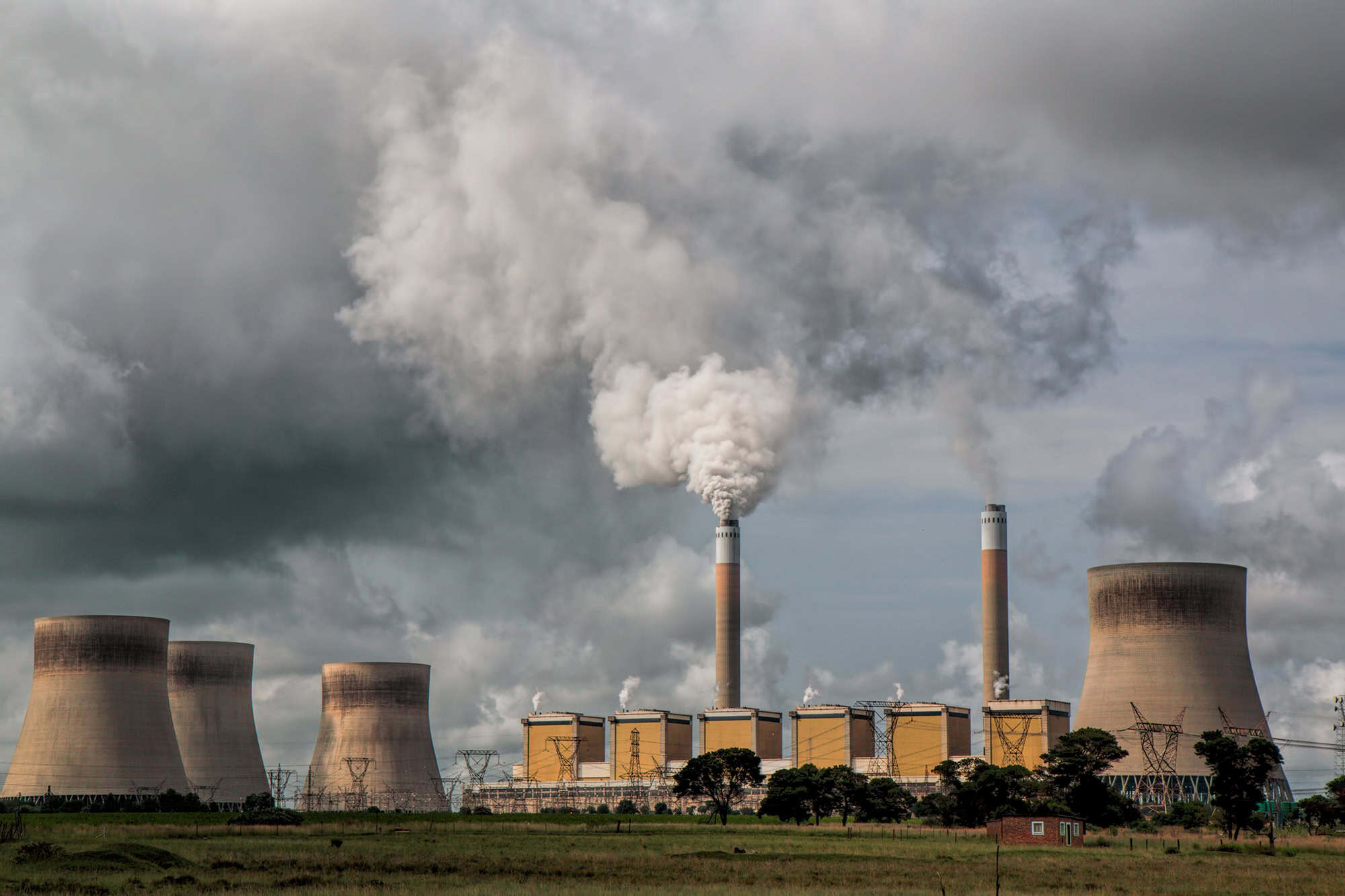 Power plant emitting smoke and steam in cloudy sky.