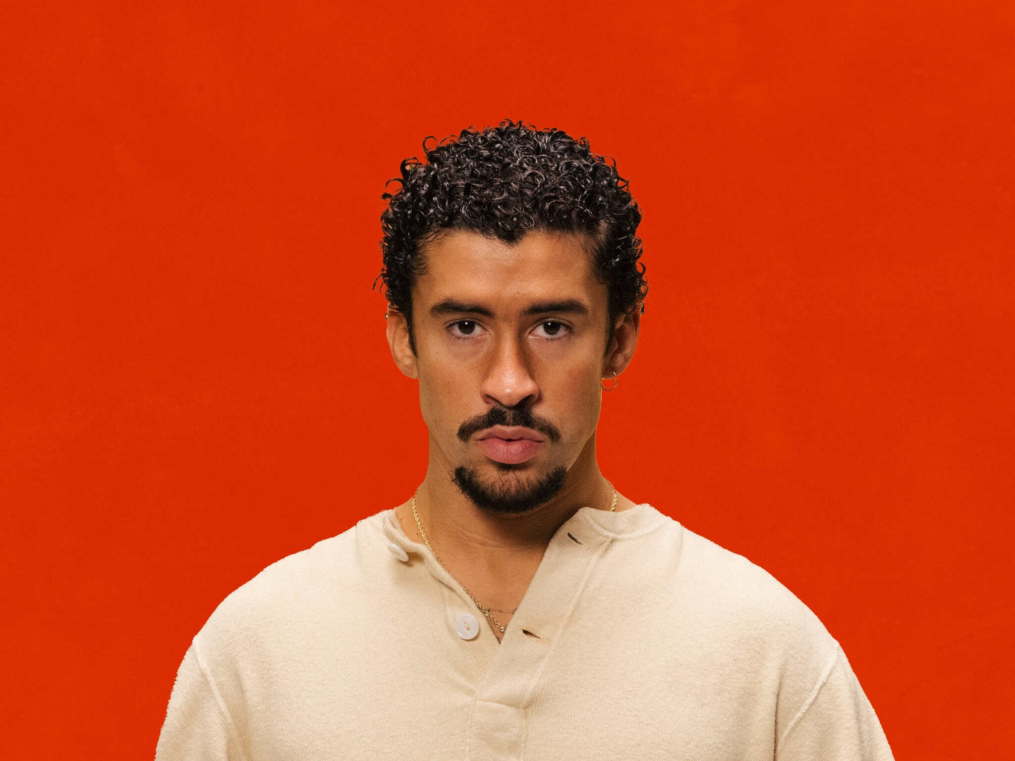 Empowered Latino man with curly hair against vibrant orange background, symbolizing leadership and c.