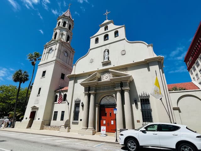 A church with a tall bell tower and classic architecture in downtown under a bright blue sky.